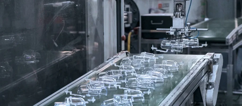 Full-automation injection molding production line with robotic pick-and-place arm continuously ejecting transparent PC optical plastic parts to conveyor system — smart manufacturing high-volume injection mold production for consumer electronics and industrial OEM supply