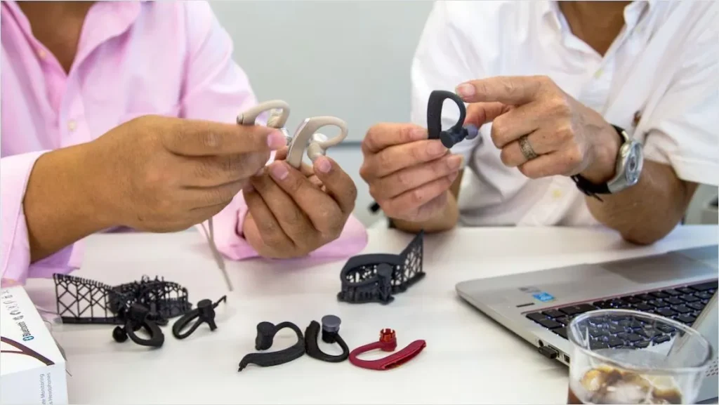 Consumer electronics product development team reviewing 3D printed rapid prototype TWS earbuds housing for custom injection mold design validation — plastic mold manufacturing for wireless earphone OEM production