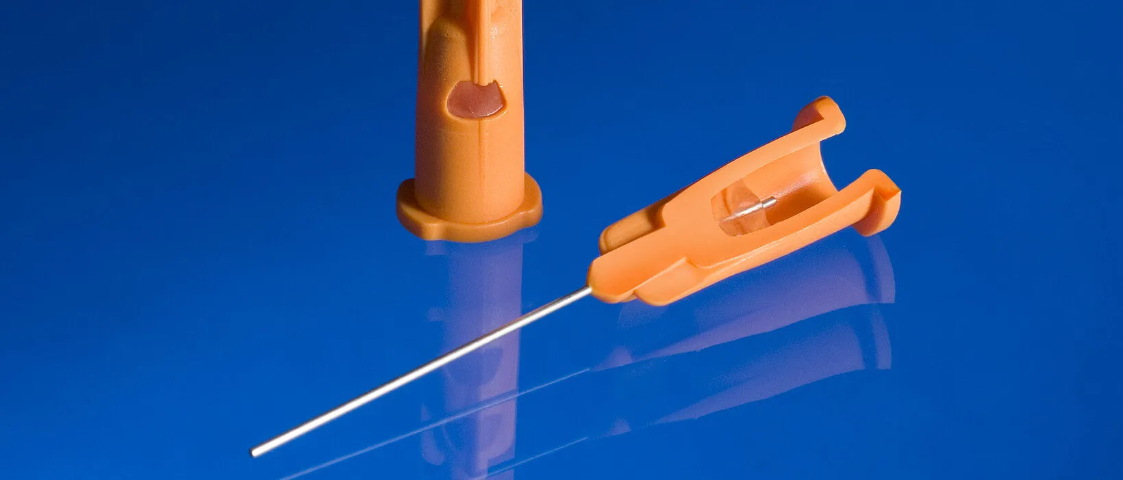 Precision insert molded stainless steel hypodermic needle cannula encapsulated in orange PP medical plastic safety hub housing — custom medical device insert molding for disposable injection needle OEM manufacturing